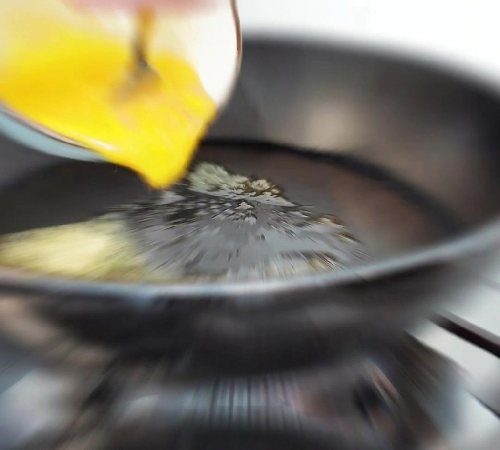 Huevo líquido batido vertiéndose desde un bol a una sartén caliente con mantequilla derretida.