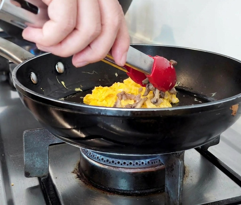 Carne picada cocinada y champiñones laminados apilados sobre una base de huevos revueltos tiernos en una sartén.