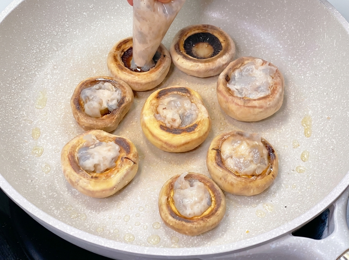 Una manga pastelera rellenando el centro hueco de un champiñón sellado con una pasta de camarón suave y traslúcida.