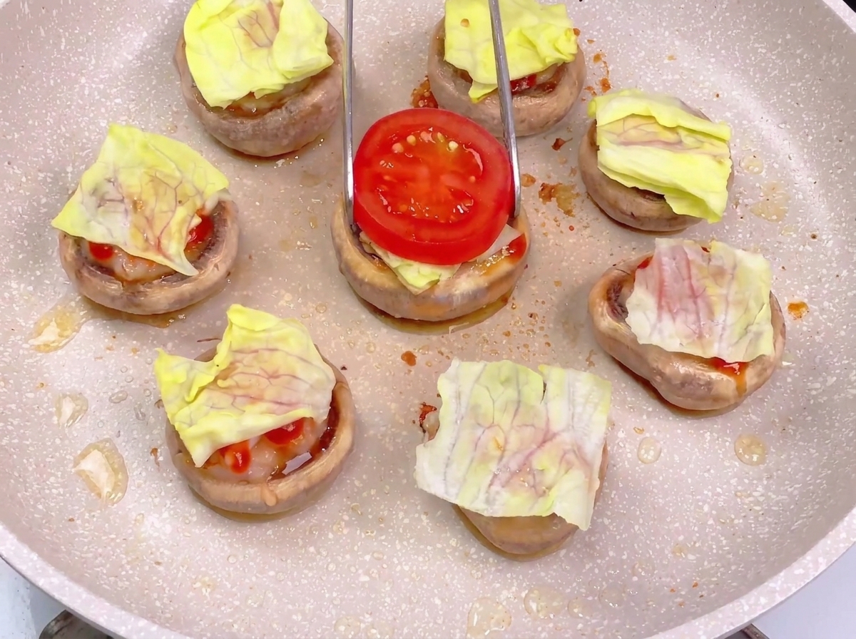 Usando unas pinzas para colocar una rodaja de tomate rojo brillante sobre una base de hamburguesa de champiñón ya montada con lechuga y salsas.
