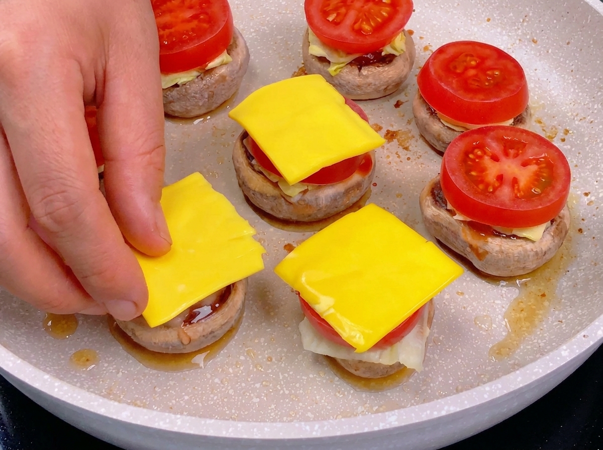 Una mano colocando un cuadrado de queso amarillo sobre una rodaja de tomate como parte del montaje de la hamburguesa.