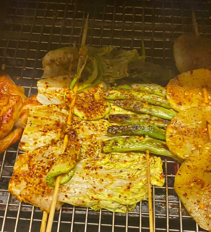 Primer plano de pollo, col y calabacín a la parrilla siendo untados con salsa BBQ roja y decorados con cebollín.