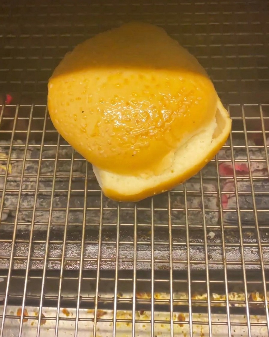 Un pan de hamburguesa sobre las brasas calientes de una parrilla para tostarse.
