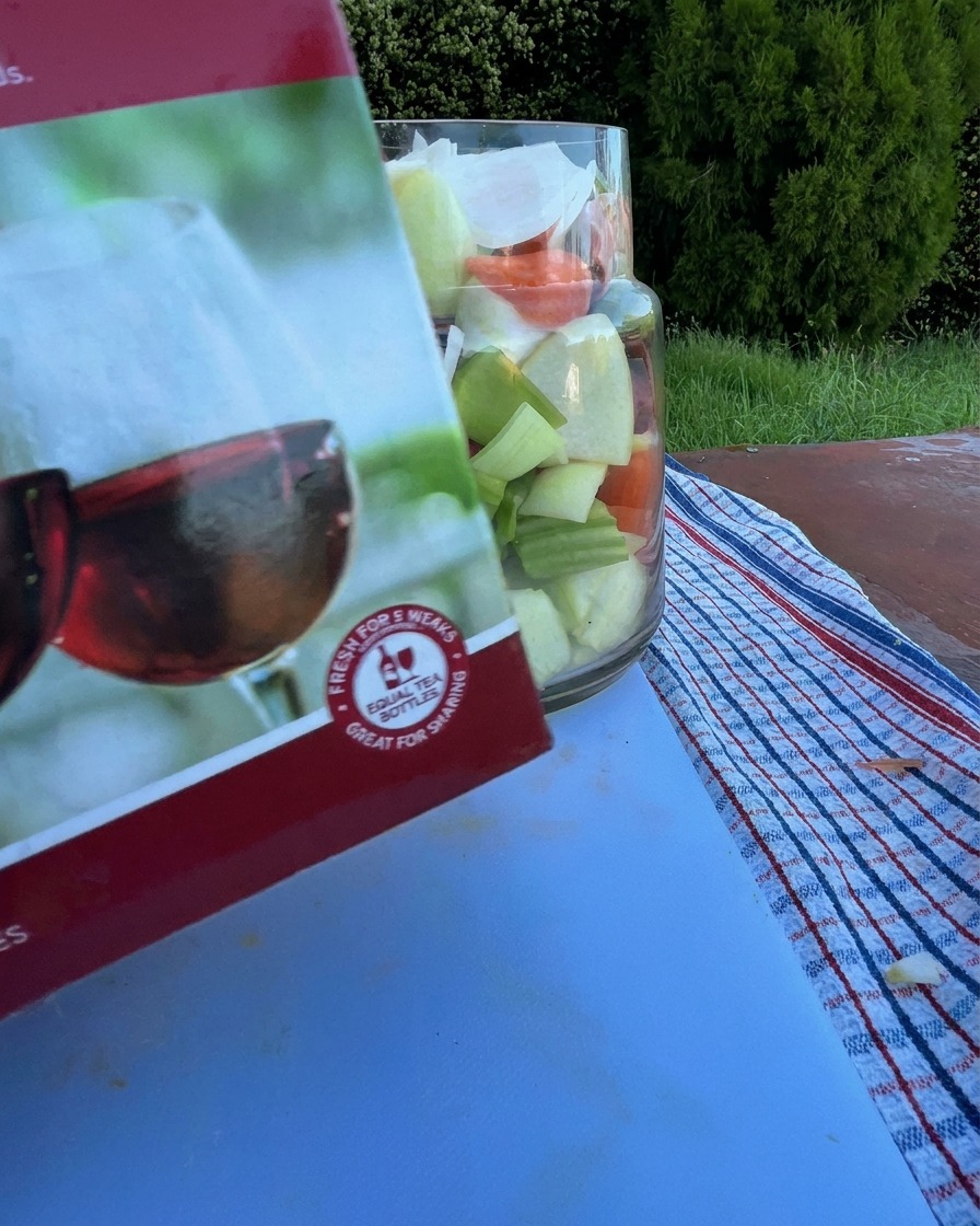 Vino tinto vertiéndose desde una caja en un frasco de vidrio que contiene costillas de res crudas y vegetales picados.