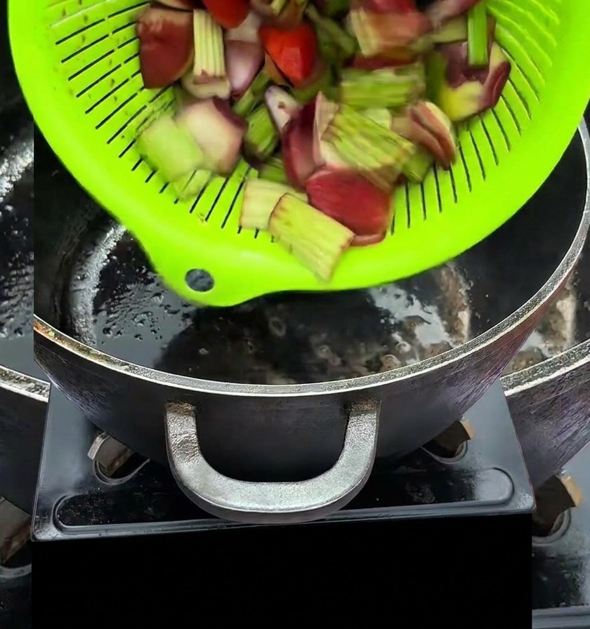 Vegetales picados vertiéndose desde un colador verde brillante en una olla negra caliente.