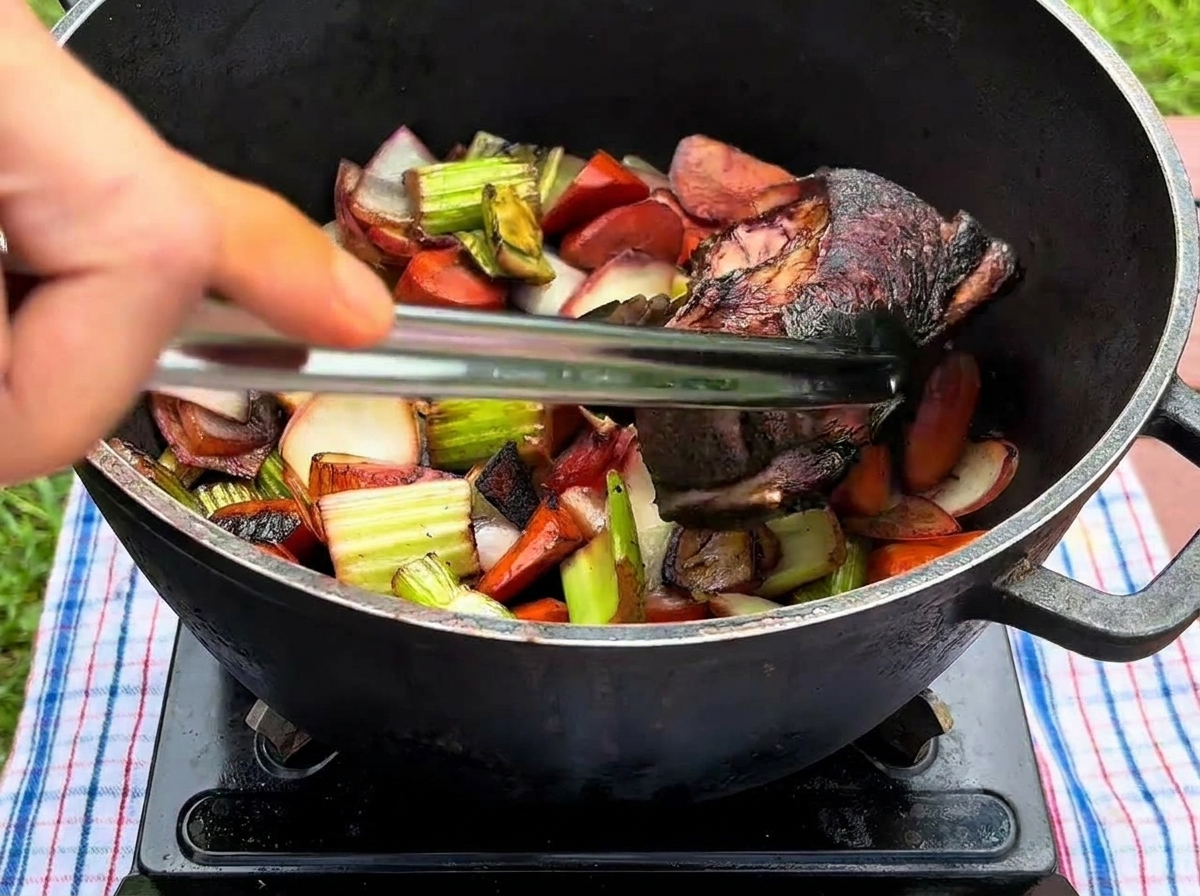 Una mano usando pinzas de metal para colocar una costilla de res sellada en una olla negra con vegetales salteados.