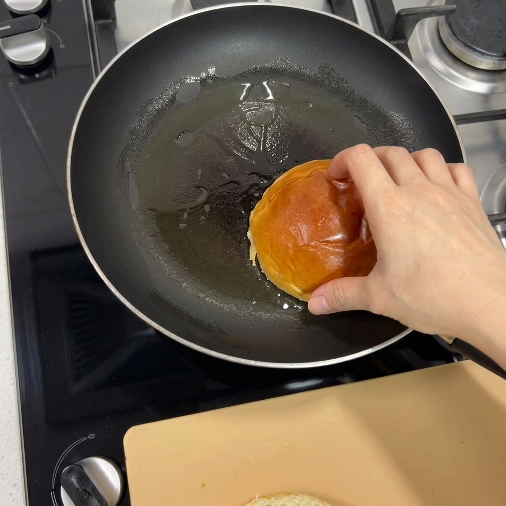 Una mano colocando un pan brioche en una sartén caliente para tostarlo hasta que quede dorado.
