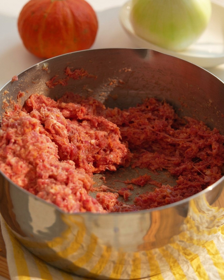 Un bol metálico con carne picada de ternera, cebolla picada y el resto de ingredientes para formar las hamburguesas.