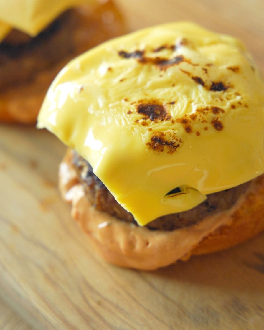 Primer plano de una loncha de queso amarillo perfectamente fundida y ligeramente tostada sobre una hamburguesa gruesa.