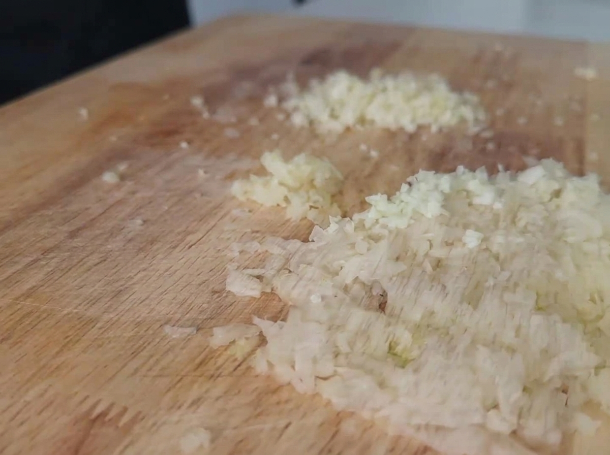 Cebolla blanca y ajo finamente picados distribuidos en una tabla de cortar de madera de color claro.