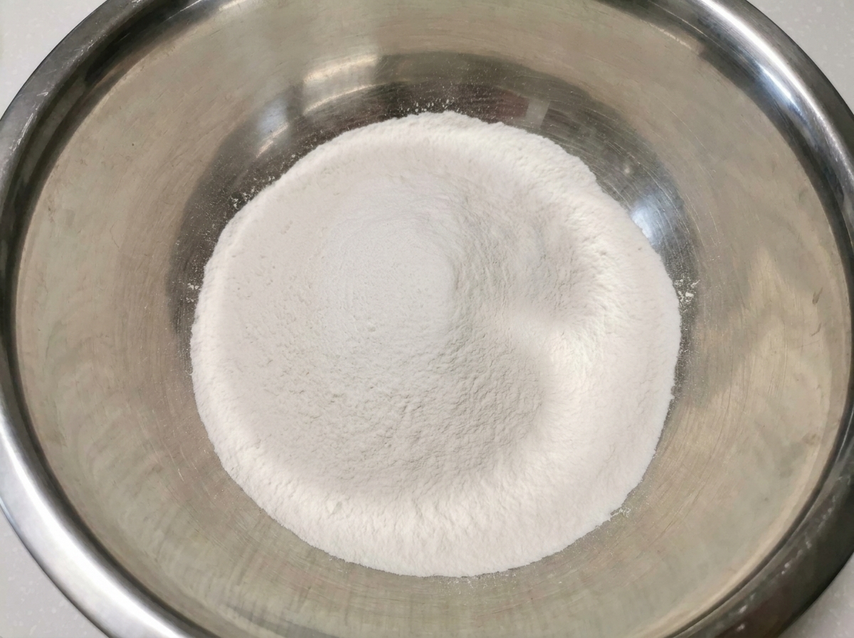 Un montículo blanco e impecable de harina de arroz mezclada con harina para todo uso dentro de un tazón grande y limpio de acero inoxidable.