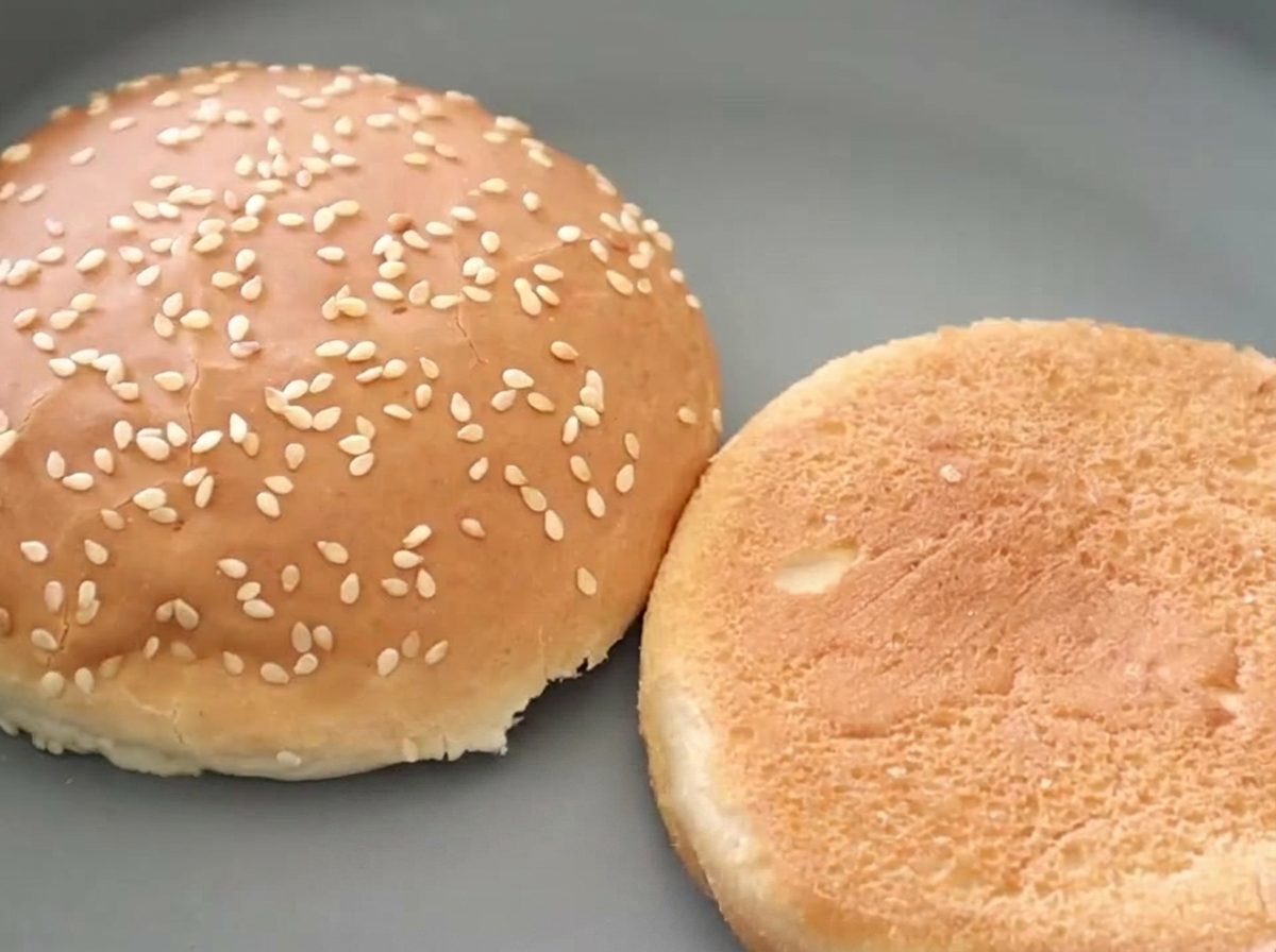Dos mitades de pan de hamburguesa con sésamo, una de ellas mostrando un interior perfectamente tostado y dorado.
