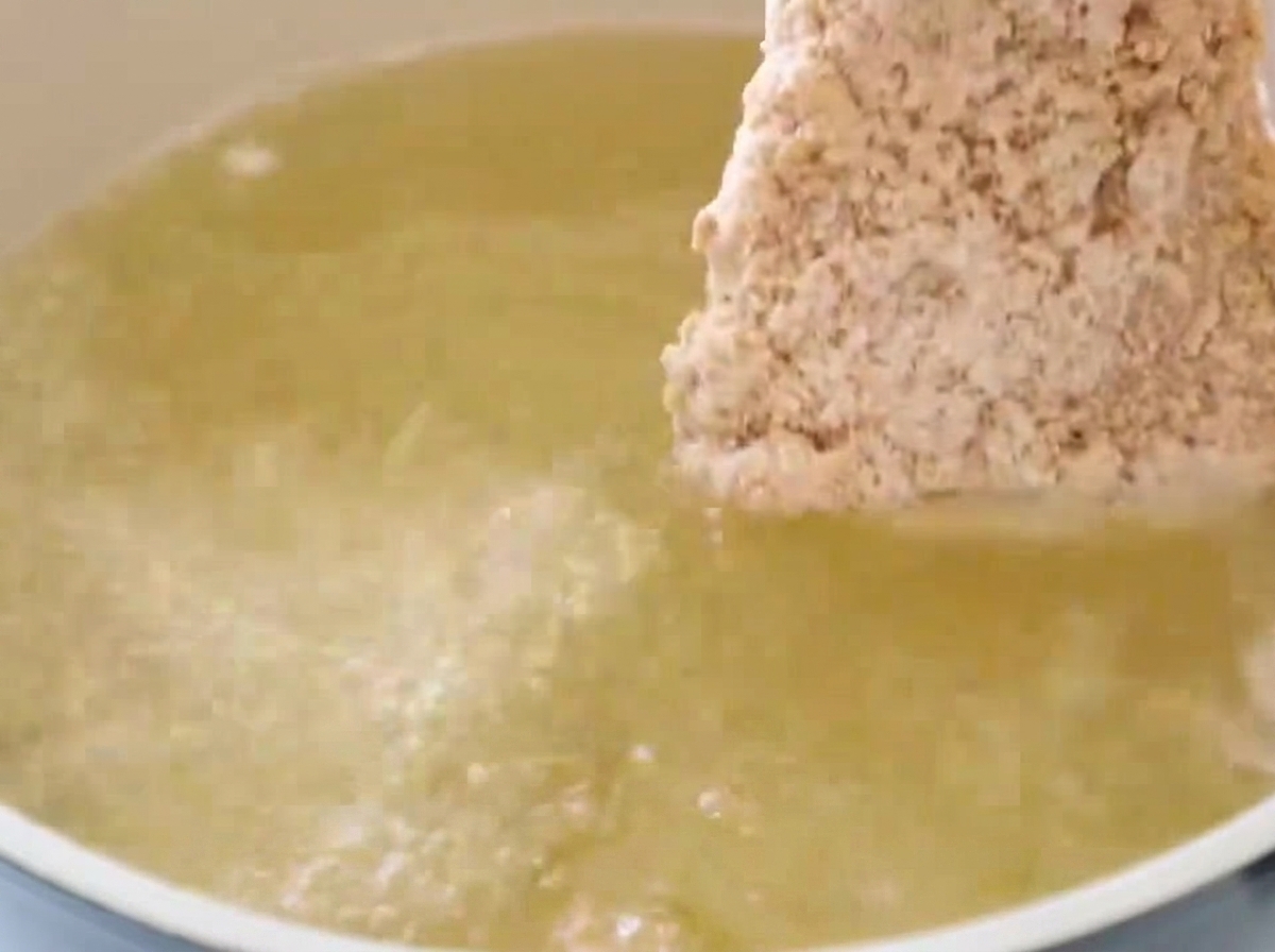 Un filete de pollo empanado sumergiéndose en una olla con aceite caliente y burbujeante.