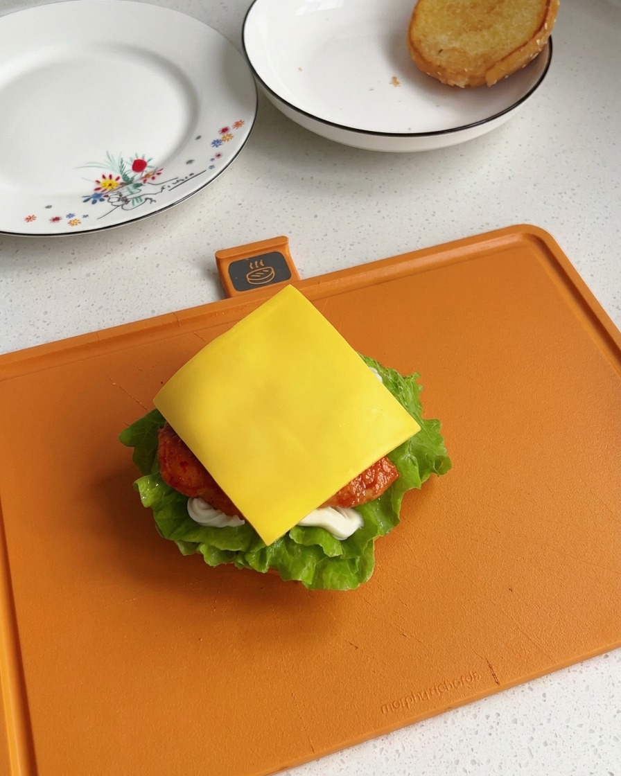Una rebanada cuadrada de queso procesado de color amarillo brillante descansando sobre un trozo de pollo recién cocinado dentro de una hamburguesa parcialmente armada.