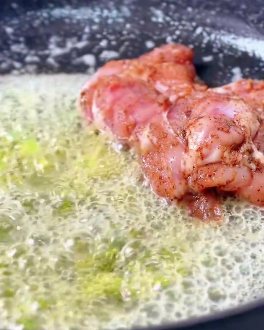 Contramuslos de pollo cajún marinados dorándose en una sartén llena de una cantidad generosa de mantequilla derretida que burbujea y hace espuma.