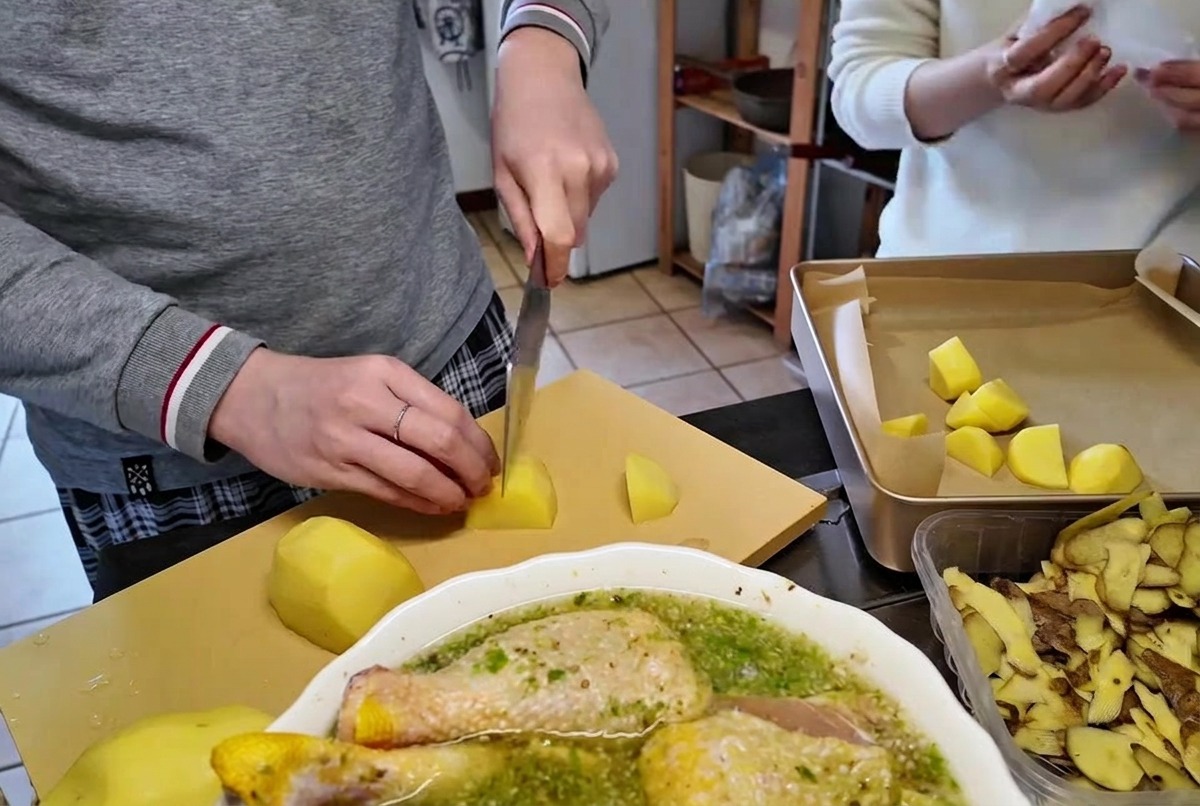 Cortando patatas crudas peladas en dados del tamaño de un bocado sobre una tabla de cortar de madera con un cuchillo afilado.