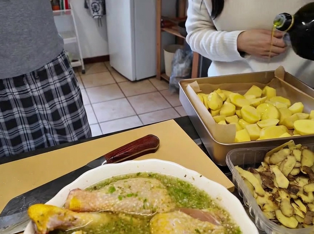 Vertiendo aceite de oliva desde una botella de cristal sobre una bandeja de horno llena de patatas troceadas.