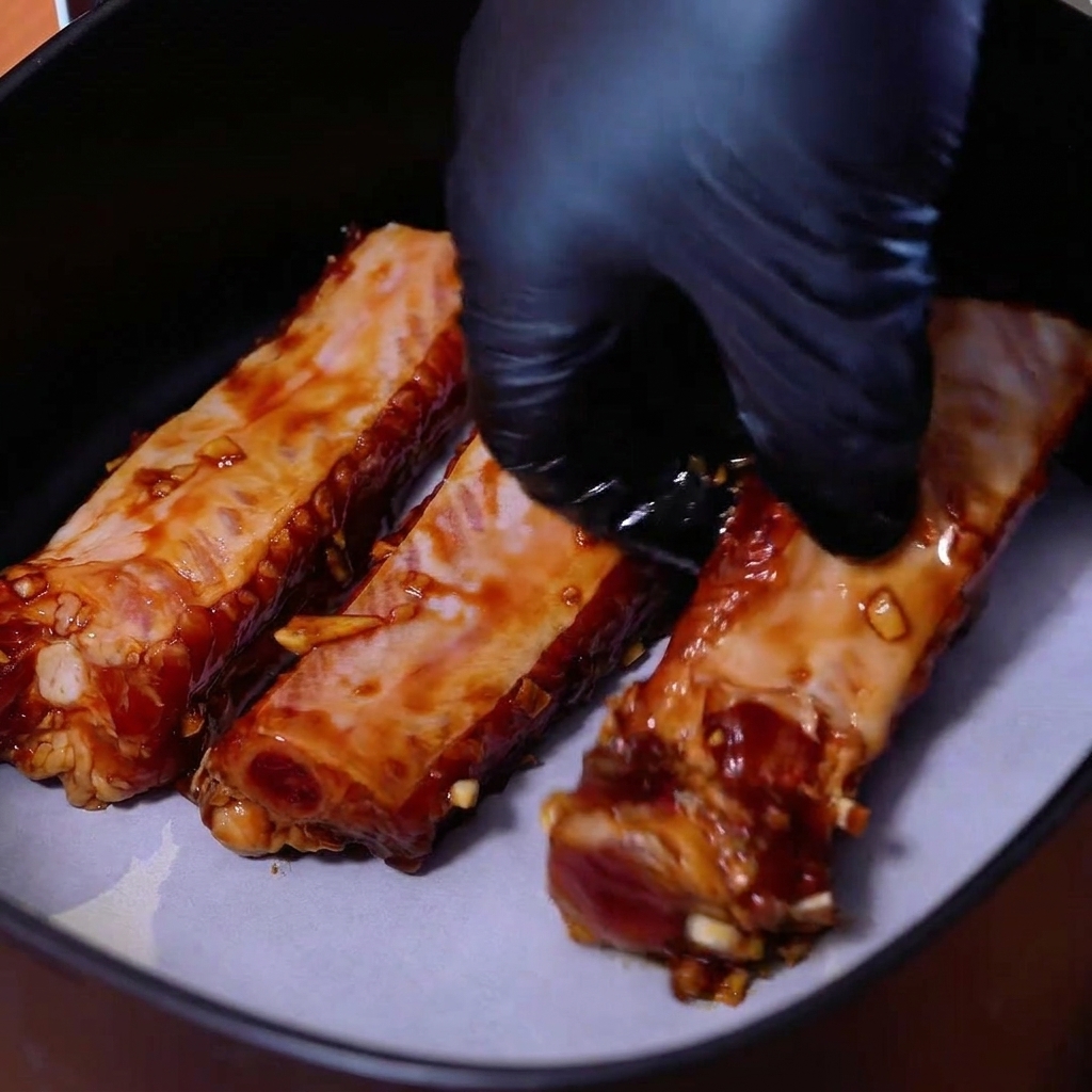 Costillas de cerdo marinadas dispuestas ordenadamente una al lado de la otra sobre papel para hornear dentro de la cesta de una freidora de aire.