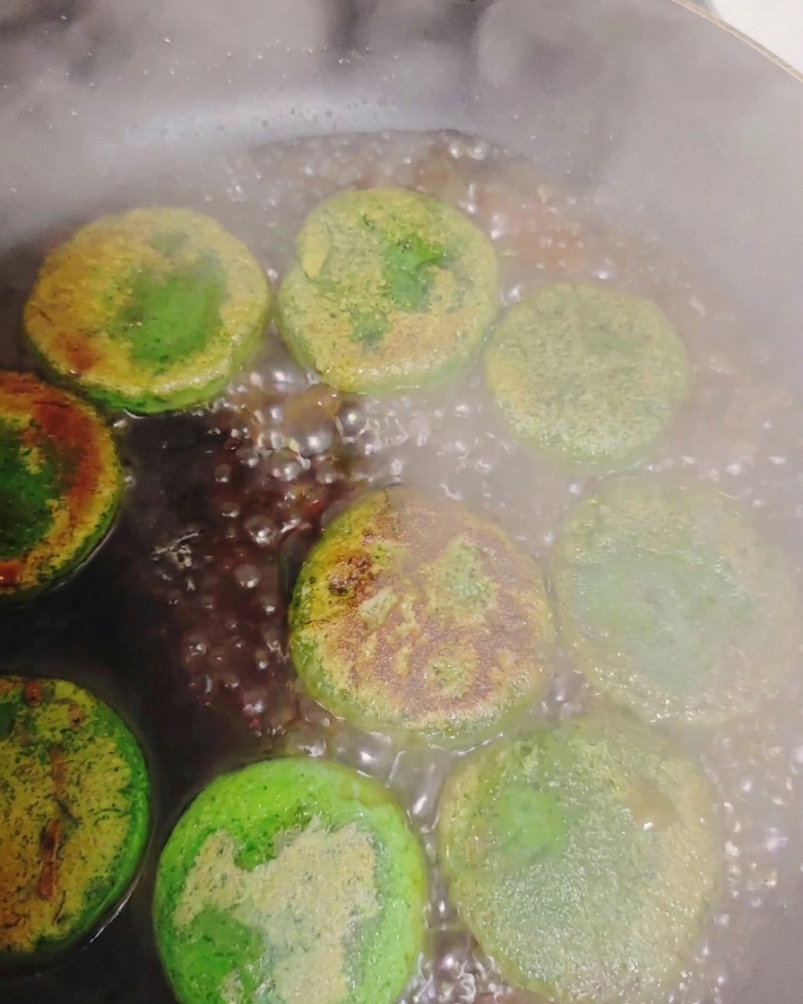 Agua burbujeando y creando vapor alrededor de las tortitas de verdura verde doradas dentro de una sartén caliente.