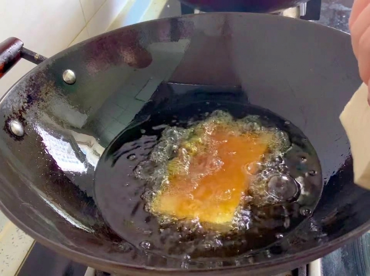 Bloques de tofu firme friéndose en un wok con aceite caliente burbujeante.