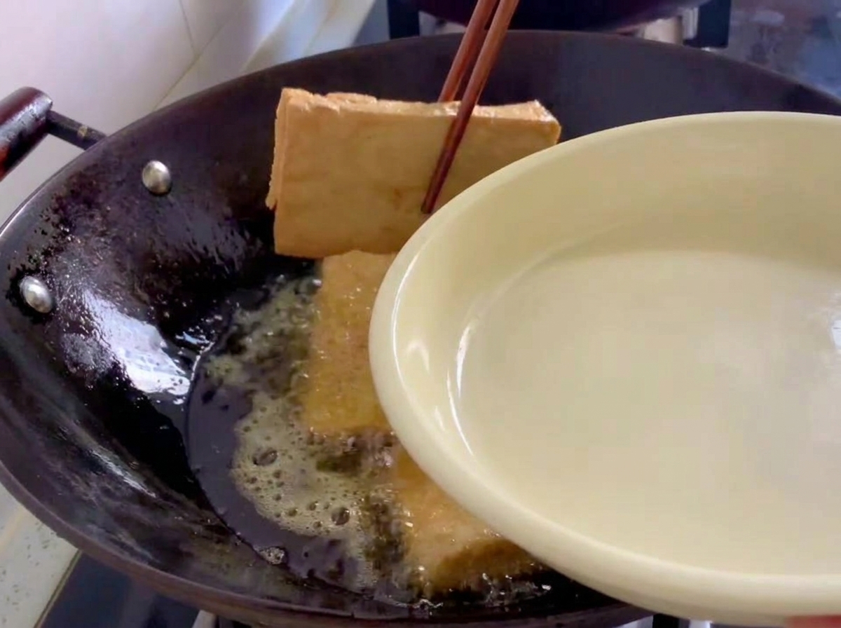 Bloques de tofu frito de color marrón dorado siendo retirados de un wok con palillos de madera.