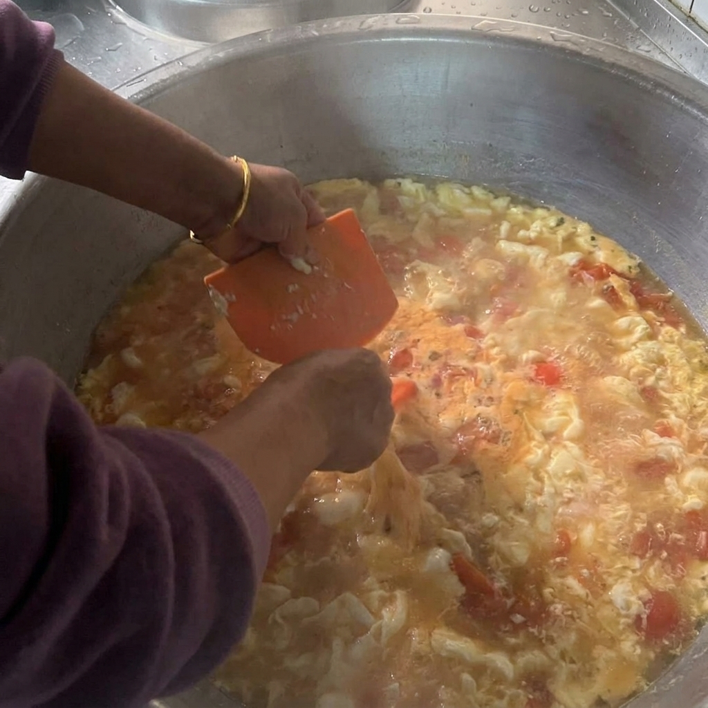 Manos sosteniendo un raspador de plástico naranja para dejar caer pequeños trozos de masa húmeda en una gran olla llena de sopa de tomate hirviendo.