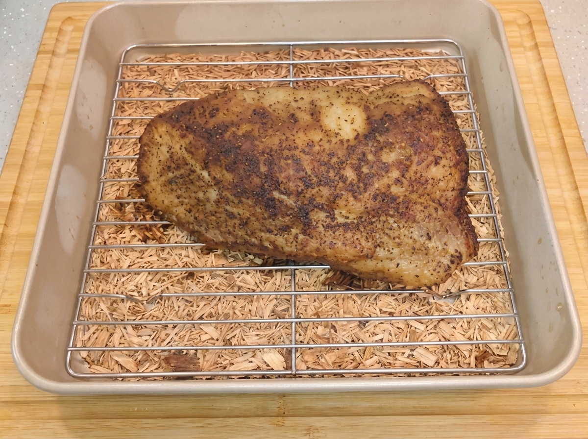 Un brisket ahumado caliente reposando sobre una rejilla de metal dentro de un molde para hornear después de retirar el papel aluminio.