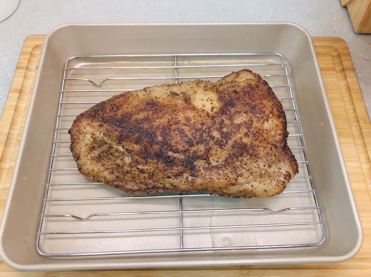 Un brisket sellado reposando sobre una rejilla dentro de una bandeja para hornear con una capa de agua en el fondo.