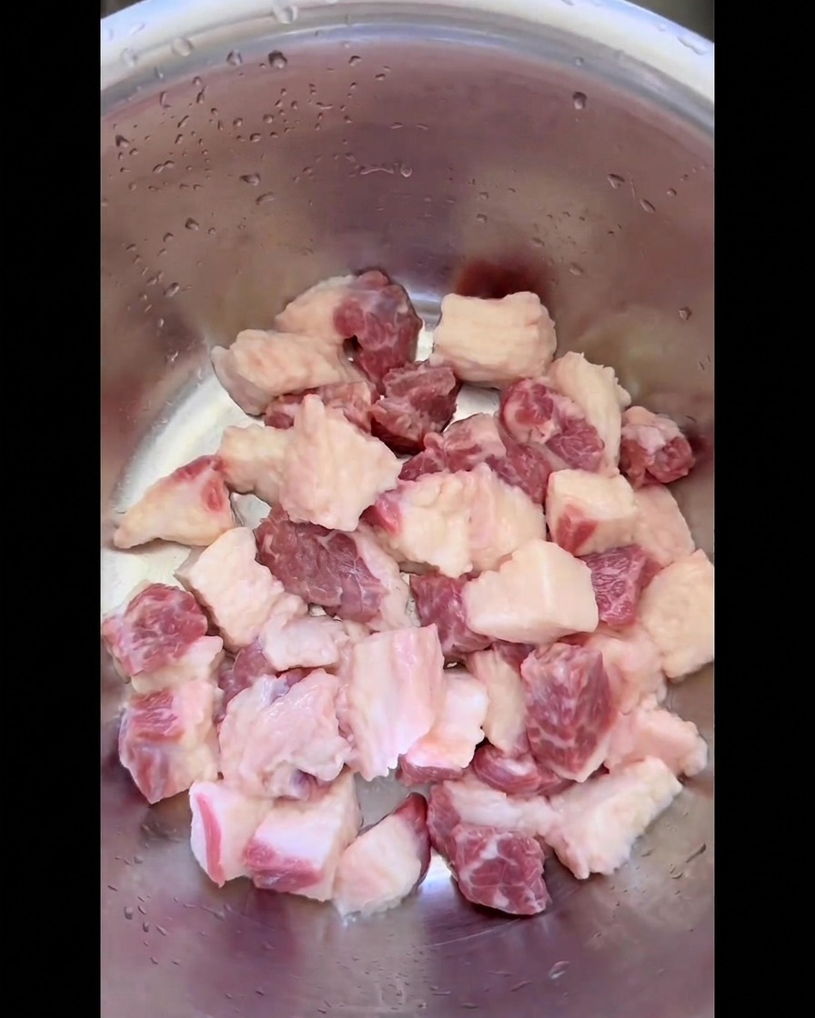 Grasa cruda de falda de res cortada limpiamente en cubos uniformes dentro de un tazón de acero inoxidable.