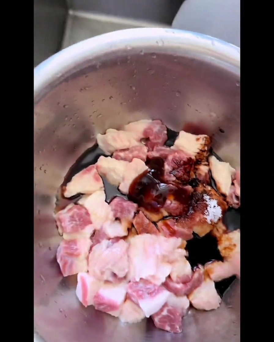 Trozos de grasa cruda de res en un tazón de acero inoxidable mezclándose a mano con salsas oscuras, azúcar y sal.