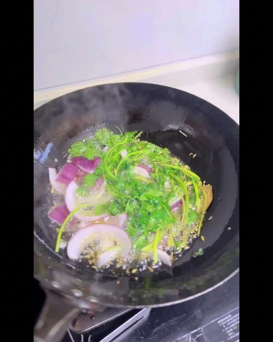 Tallos de cilantro fresco y cebolla morada rebanada chisporroteando dentro de un wok lleno de aceite caliente brillante.
