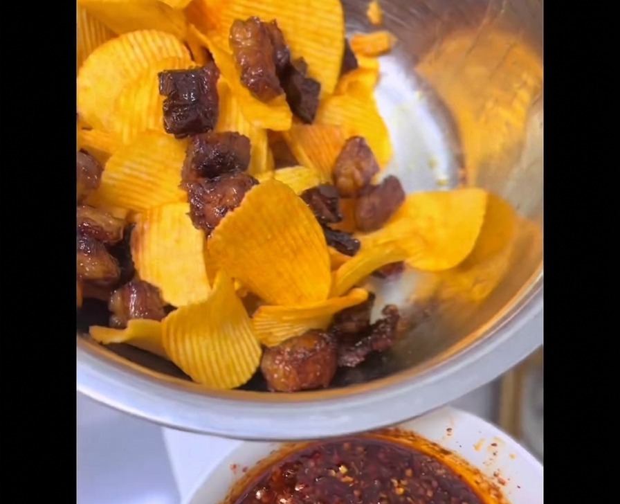 Trozos crujientes de grasa de res hechos en freidora de aire mezclados con papas fritas onduladas de color amarillo brillante dentro de un tazón de acero inoxidable.