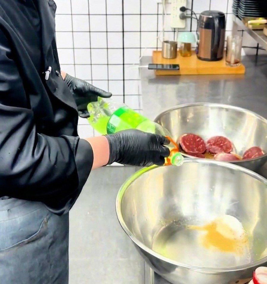 Un cocinero vertiendo un líquido claro desde una botella en un bol de acero inoxidable que contiene los condimentos en polvo.