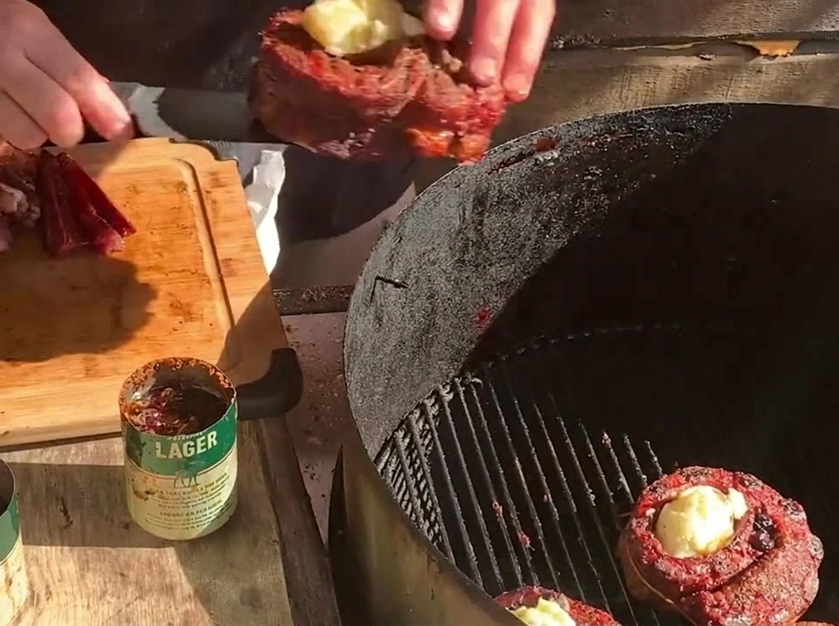 Colocando una copa de costilla rellena en una parrilla de carbón junto a otra copa de carne y lonchas gruesas de bacon.