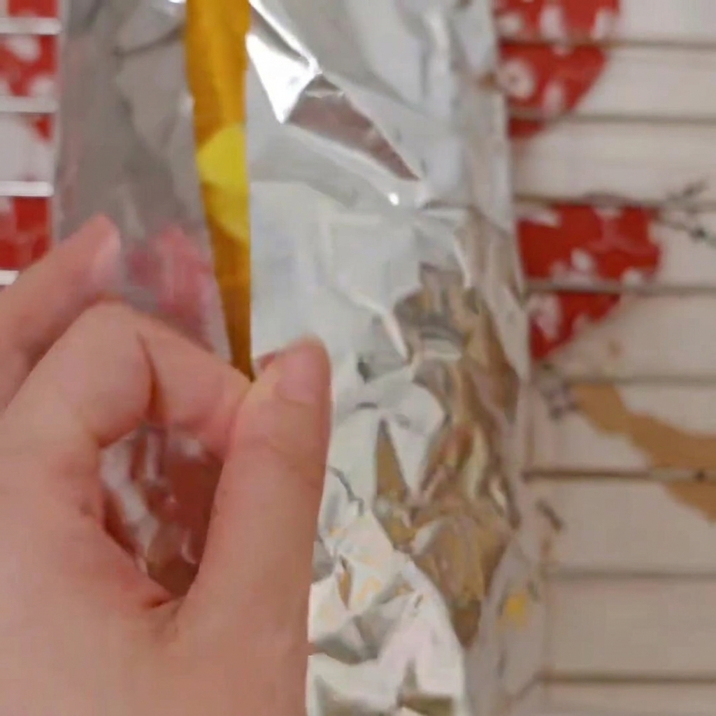 Dedos doblando y envolviendo mazorcas de maíz dulce dentro de una hoja de papel de aluminio plateado.