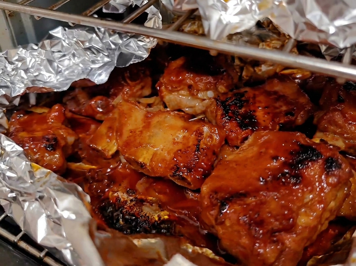 Costillas de cerdo horneadas y profundamente caramelizadas burbujeando dentro de un envoltorio de papel de aluminio abierto en el horno.