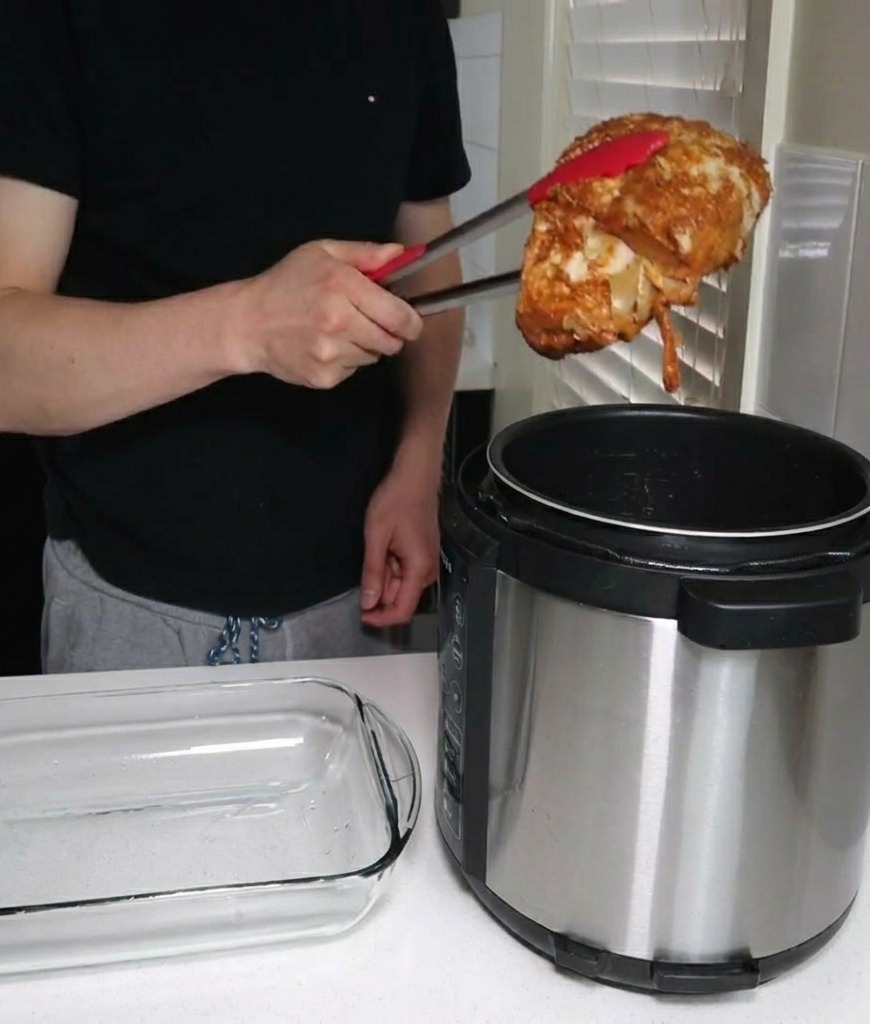 Una persona usa pinzas de cocina con puntas rojas para sacar un trozo grande de cerdo cocido de una olla a presión junto a una fuente de vidrio vacía.