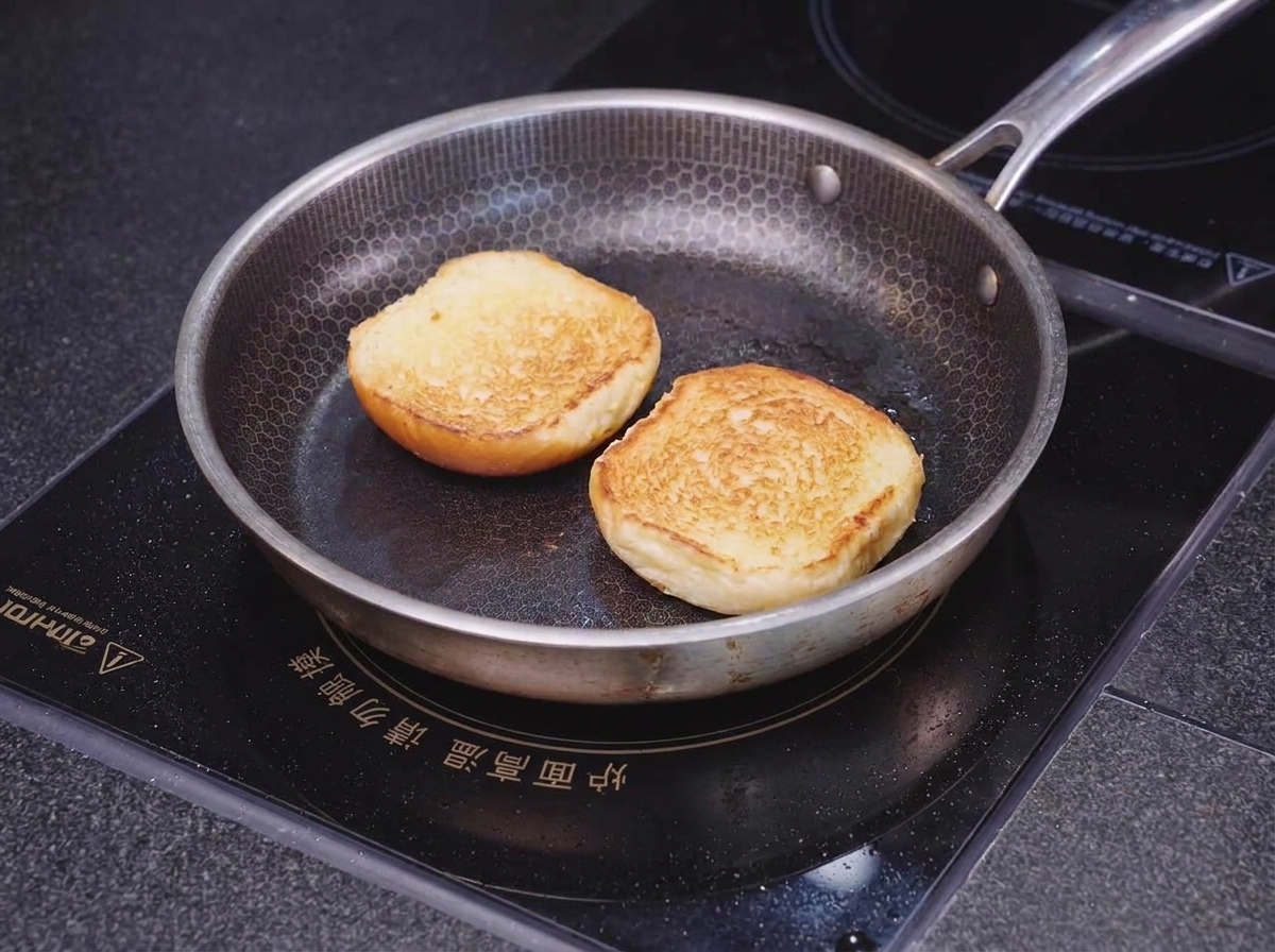 Dos mitades de un pan brioche tostándose boca abajo en una sartén con dibujo de panal hasta que los bordes queden dorados y crujientes.