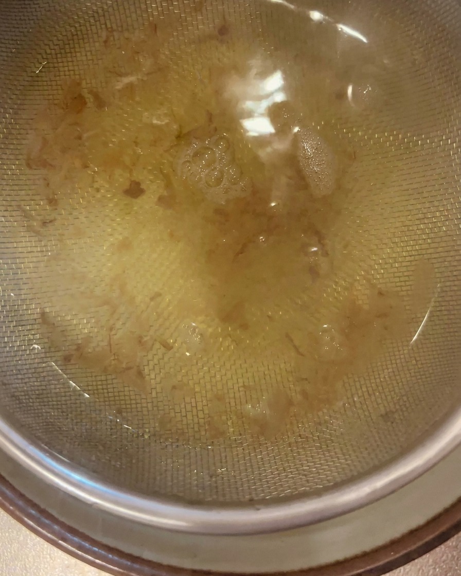 Caldo dashi de color dorado claro pasando a través de un colador de malla fina hacia un cuenco.