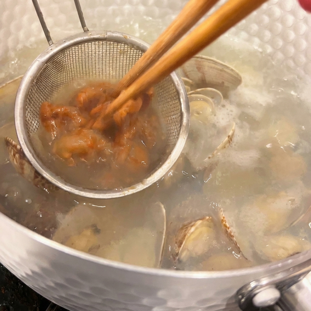 Un pequeño colador de mano con pasta miso mientras se disuelve con unos palillos en la sopa caliente con almejas.