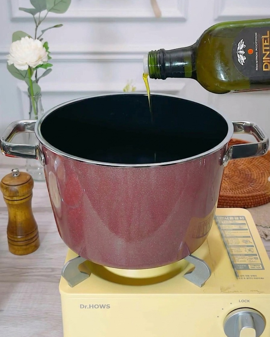 Aceite de oliva virgen extra vertiéndose en una olla de cocina vacía y precalentada.