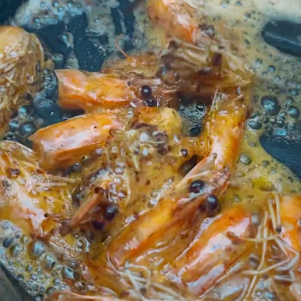 Cabezas de camarón siendo retiradas del aceite sazonado usando palillos de cocina.