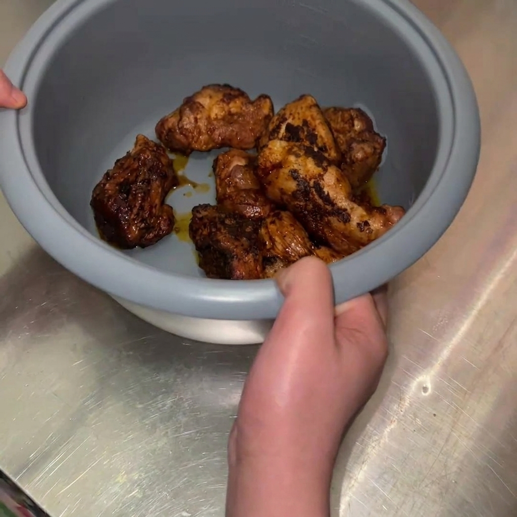 Una persona sosteniendo el bol interior gris de una olla arrocera lleno de trozos de cerdo fritos dorados.