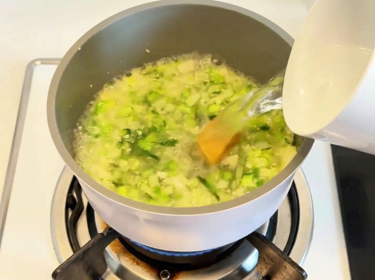 Agua vertiéndose en una olla que contiene las verduras sofritas y la base de sopa.