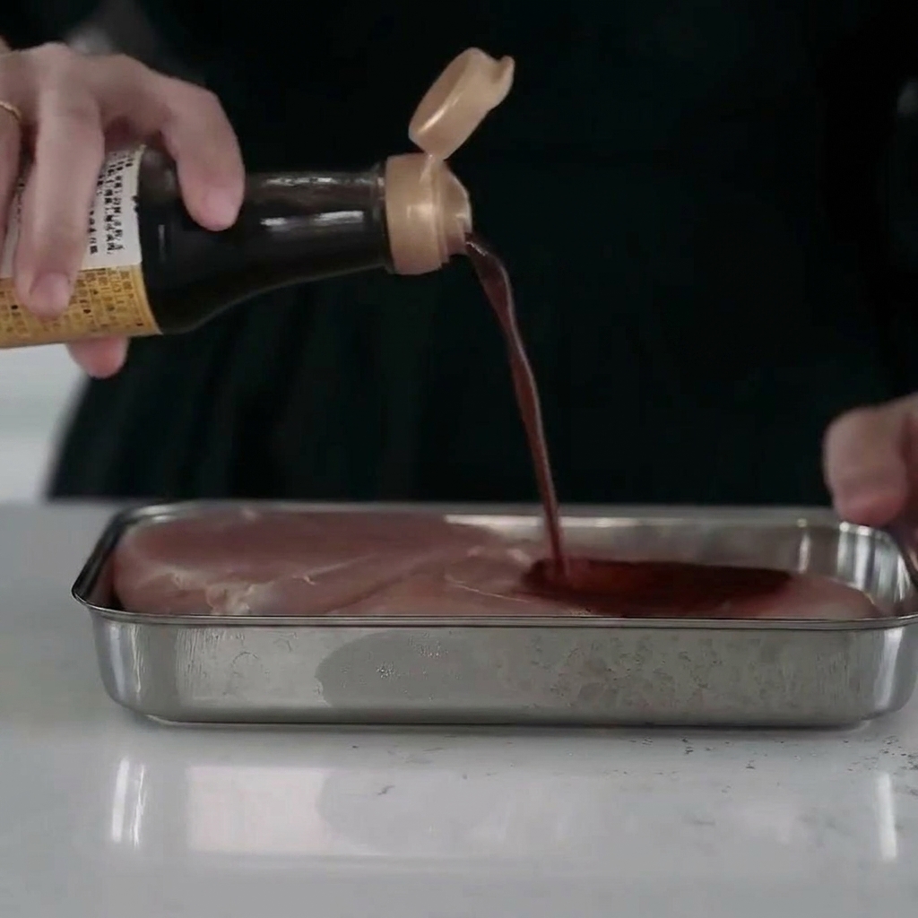 Trozos de pechuga de pollo jugosos en una bandeja de metal, cubiertos con un adobo líquido.