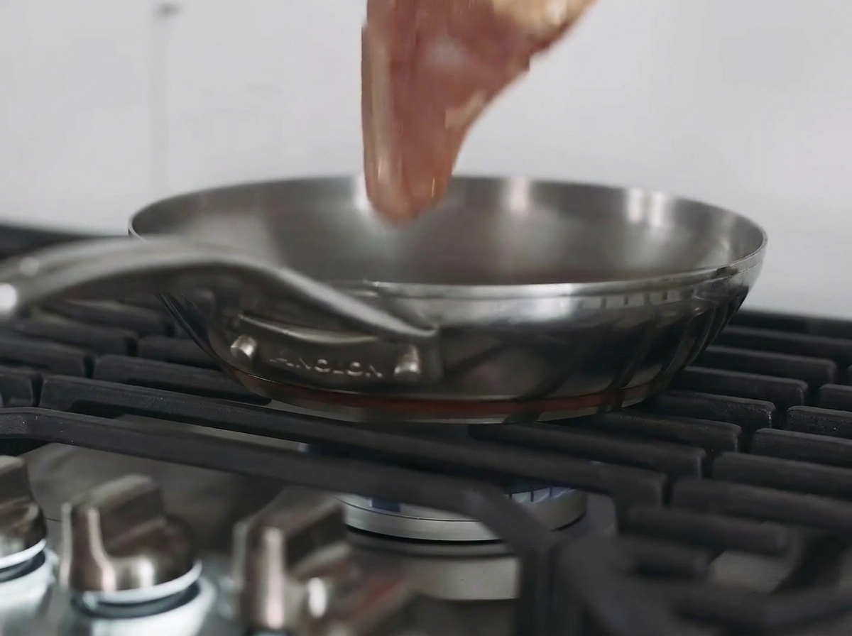 Una pechuga de pollo dorándose en una sartén de acero inoxidable sobre el fogón.