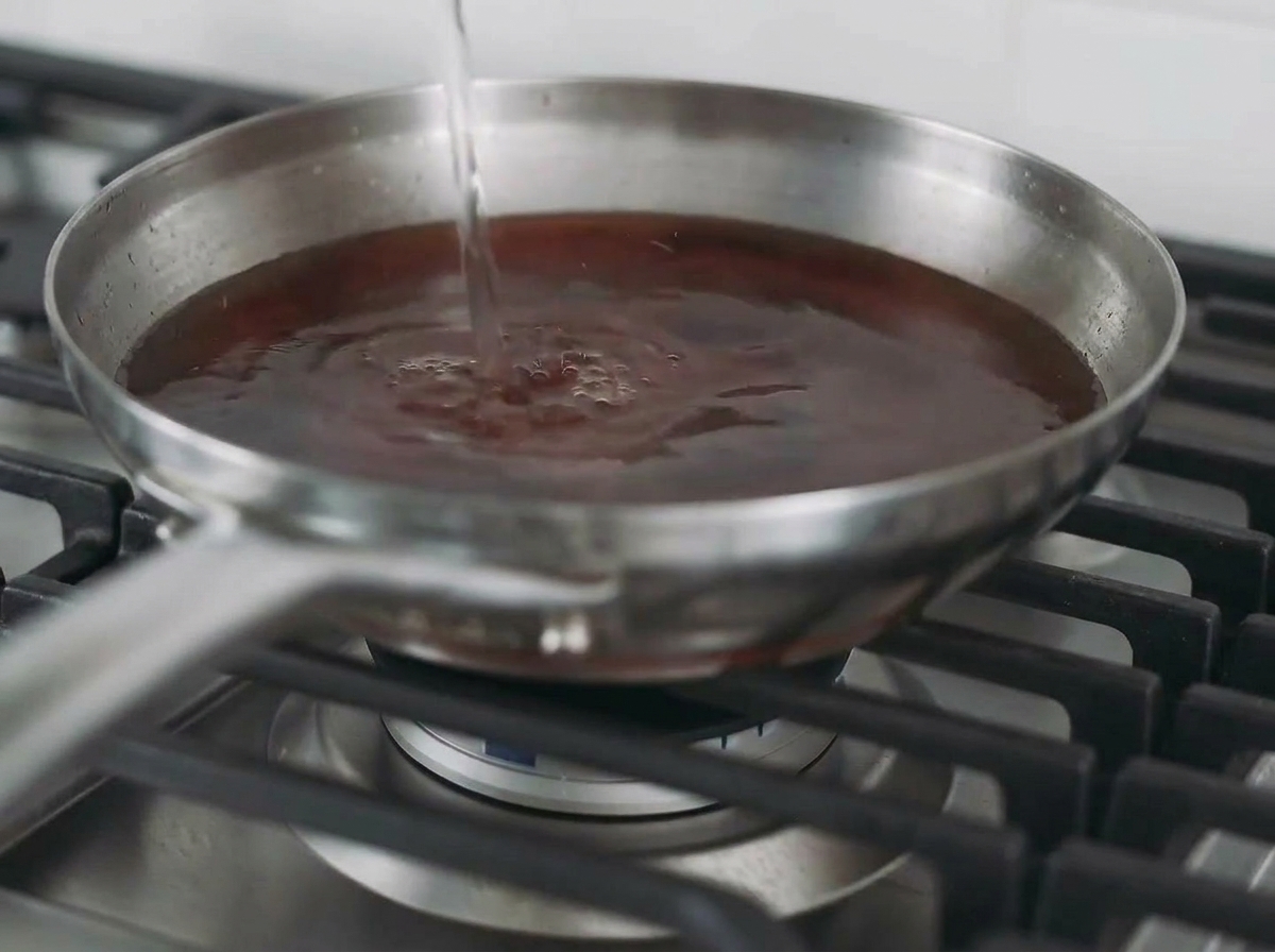 Se vierte líquido en una sartén con la pechuga de pollo dorada para crear un caldo.