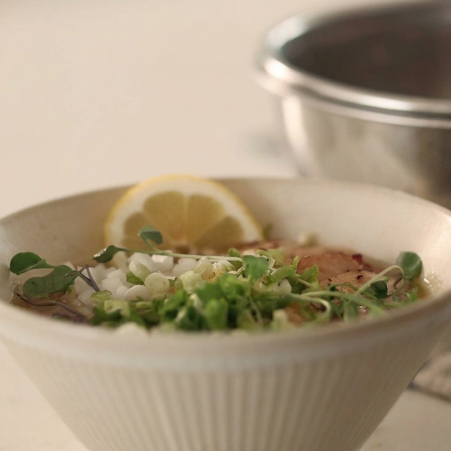 Un bol de fideos fríos en caldo cubierto con cebolla picada, cebollino y pimienta negra.