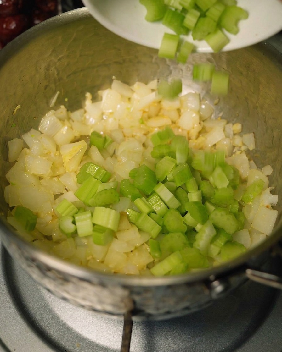 Apio y zanahorias siendo agregados a la olla con los aromáticos sofritos.