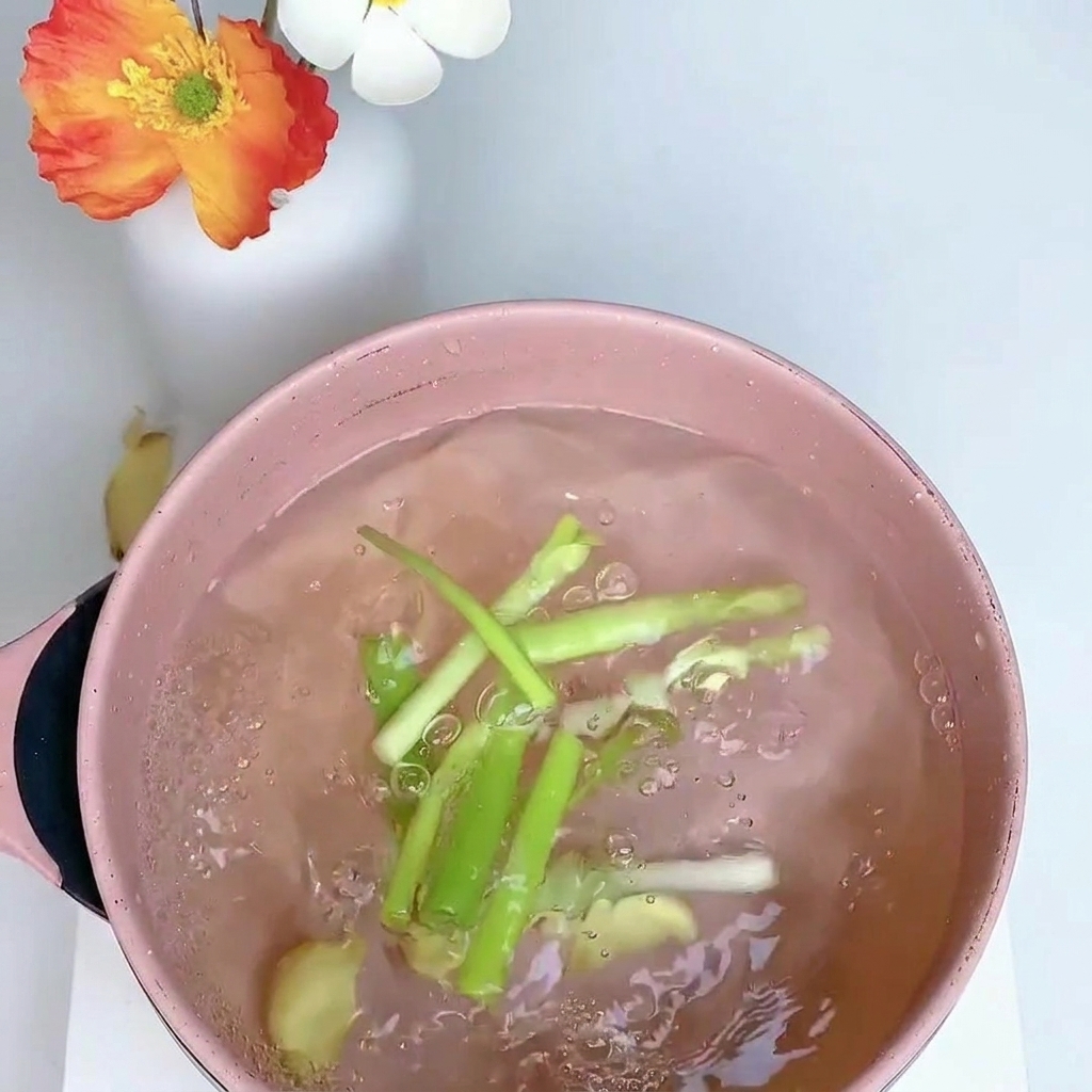 Muslo de pollo hirviendo en una olla con cebolleta, jengibre y anís estrellado.